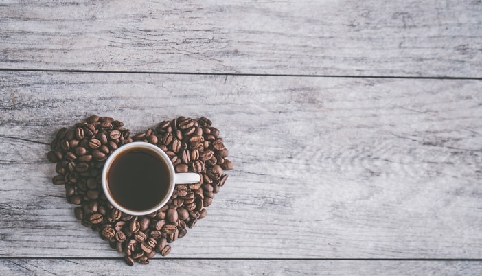 coffee beans in a heart shape with a black coffee mug in the middle
